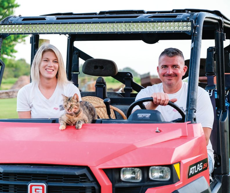 Owners of North Florida Elderberry sitting in a pink golf cart, smiling. Small cat laying on the hood
